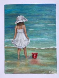 Girl with red bucket on the shore